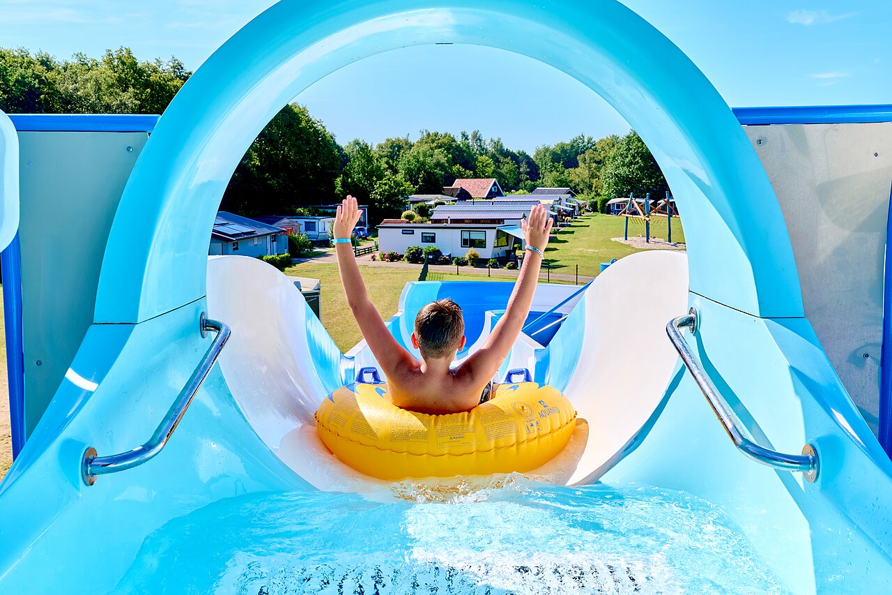 Kind auf Wasserrutsche, gelber Schwimmreifen, auf Camping CAPFUN De Eikenhof in Paasloo/Oldemarkt.