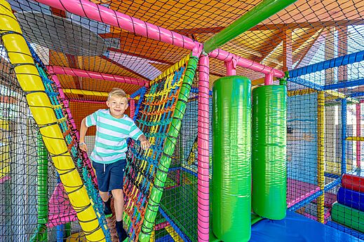 Lächelndes Kind in bunter Indoor-Spielstruktur auf dem Campingplatz CAPFUN De Eikenhof in Paasloo/Oldemarkt.