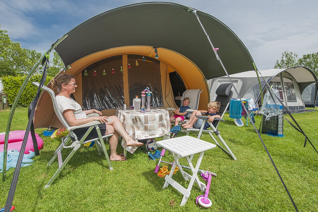 Famille se d�tendant sur un emplacement de camping avec tente et auvent au camping CAPFUN De Rotonde � Enspijk.