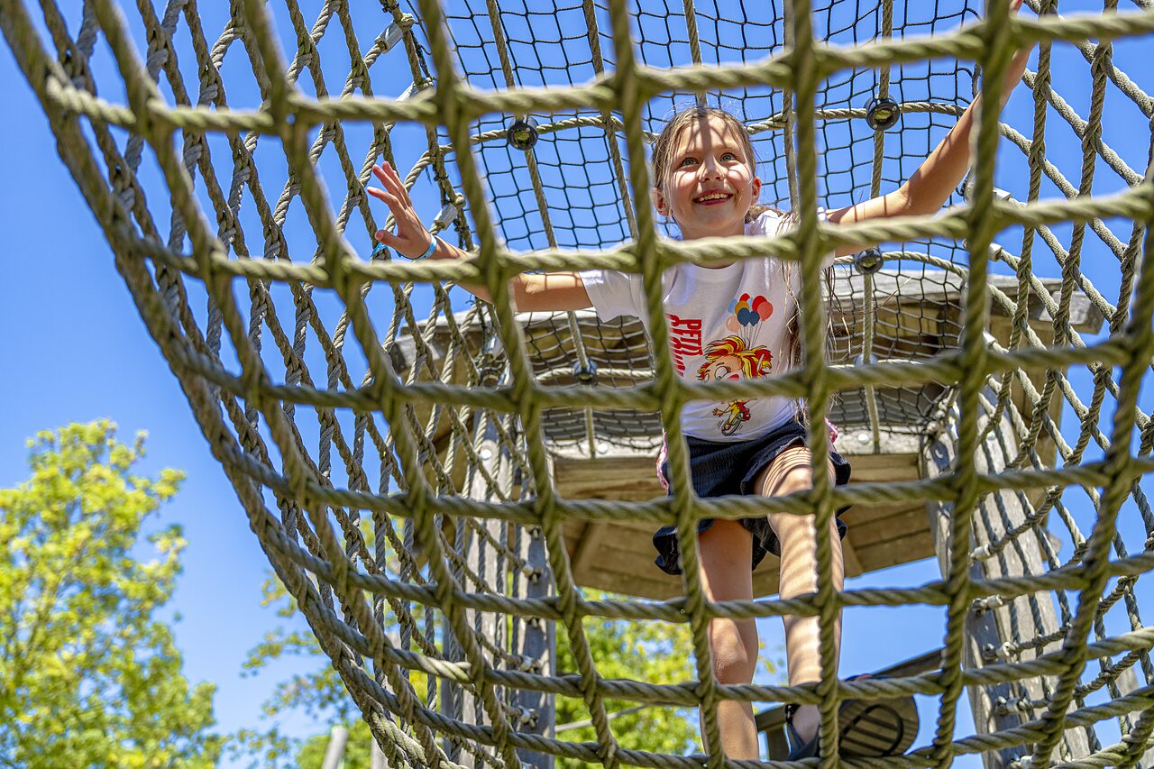 Enfant souriant grimpant sur une structure de jeux en corde au camping CAPFUN De Rotonde � Enspijk.