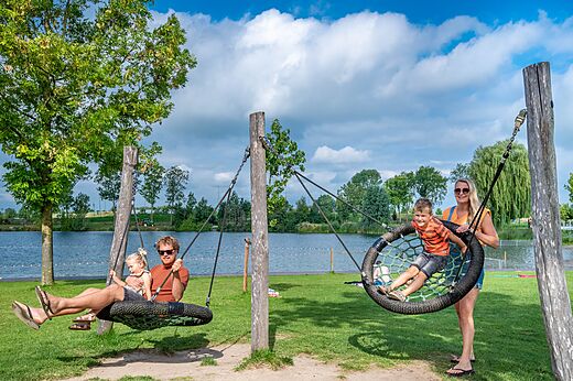 Familien auf Vogelnestschaukeln am See auf Camping CAPFUN De Rotonde.