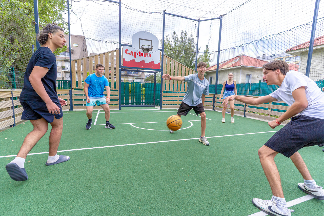 Jugendliche spielen Basketball auf dem Multisportplatz des Campingplatzes CAPFUN Donjon de Lars in Courseulles-sur-Mer.