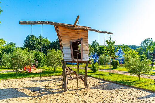 Speeltuin met houten huisje en schommels op camping CAPFUN Duravel.