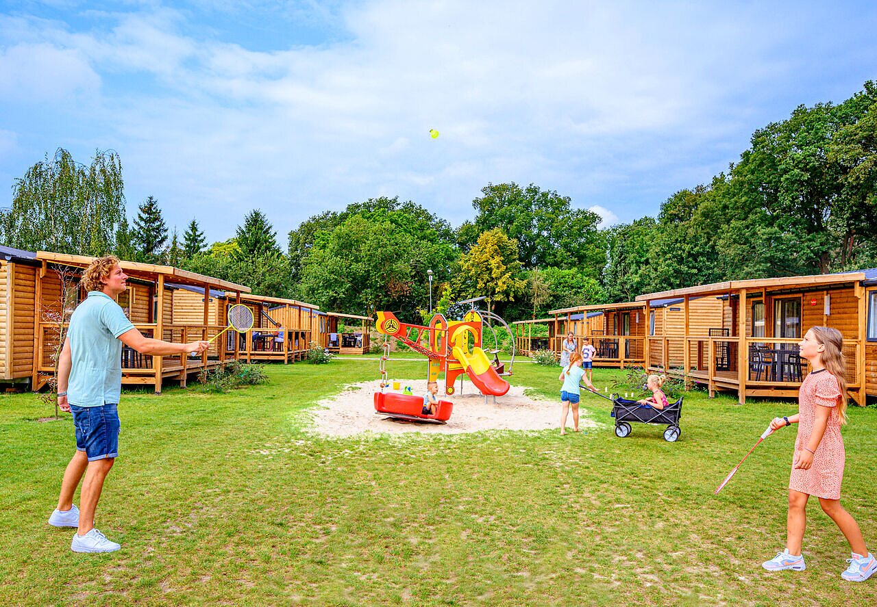Familie spielt Badminton und Kinder auf Spielplatz, Holzunterk�nfte auf Camping CAPFUN Eibernest in Eibergen.
