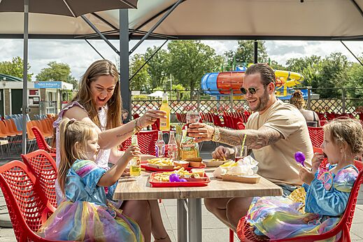 Lächelnde Familie isst auf Restaurantterrasse des Campingplatzes CAPFUN Eibernest in Eibergen.