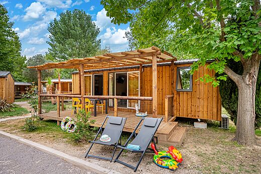 Mobil-home en bois avec terrasse couverte et chaises au camping CAPFUN El Moli à Elne (66).