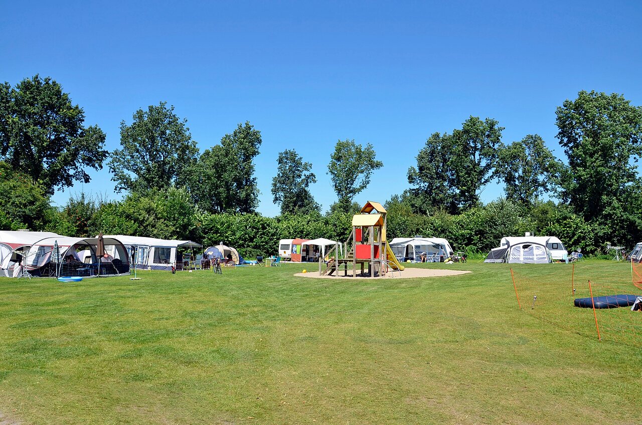 Groene kampeerplaatsen met speeltuin en caravans op camping CAPFUN Erkemederstrand in Zeewolde.