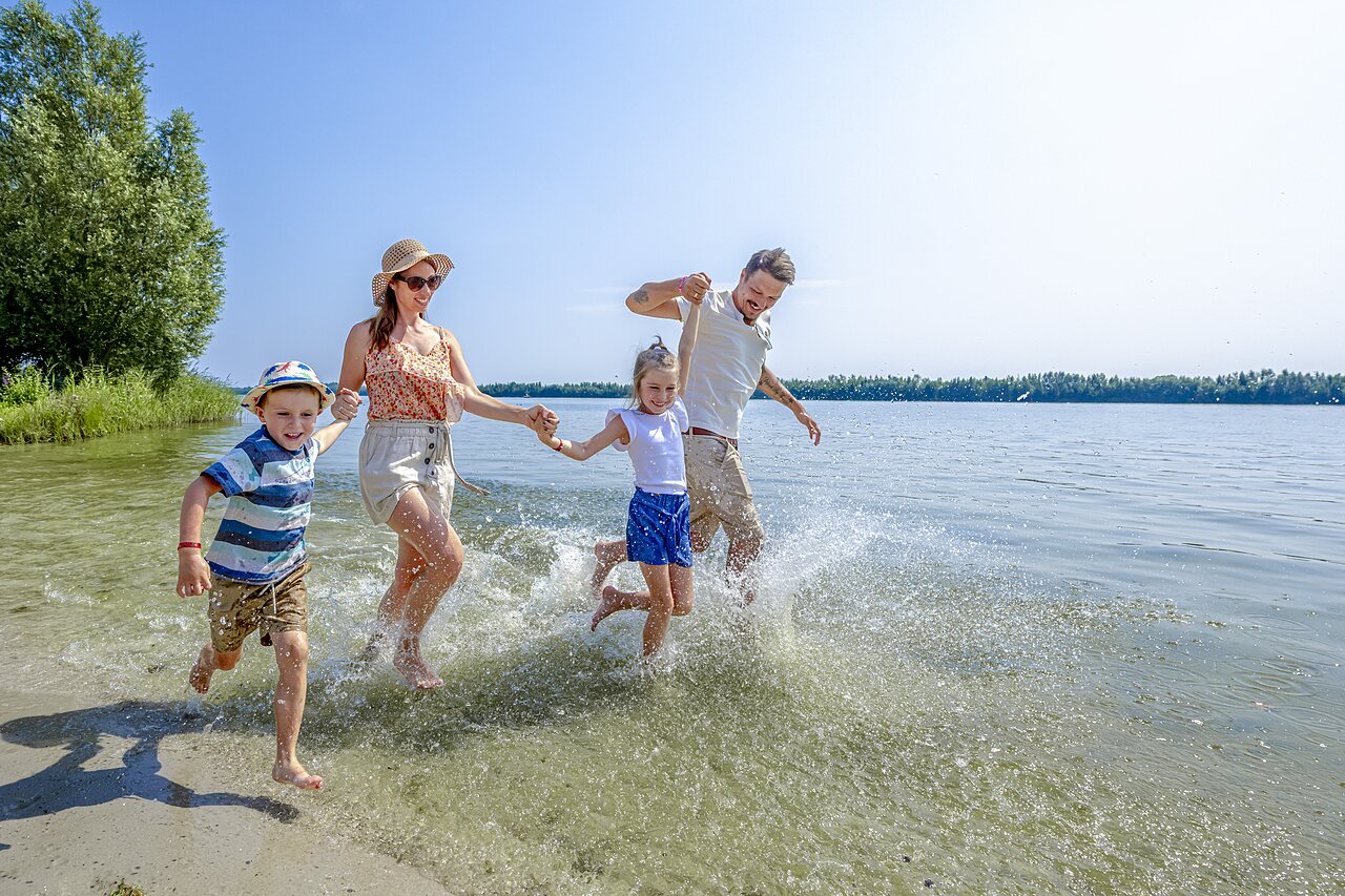 Vrolijke familie rennend en spetterend in ondiep water op camping CAPFUN Erkemederstrand in Zeewolde.
