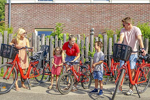 Familie mietet rote Fahrr�der mit Kindersitz auf dem Campingplatz CAPFUN Erkemederstrand in Zeewolde.