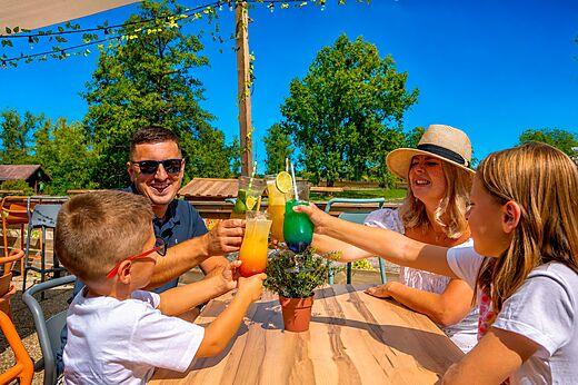 Famille souriante trinquant avec des cocktails colorés au bar du camping CLICOCHIC Etang de la Mutche à HARPRICH (57).
