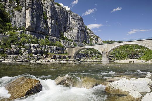 Alte Steinbrücke über Fluss, majestätische Felsenklippen, touristische Sehenswürdigkeit.