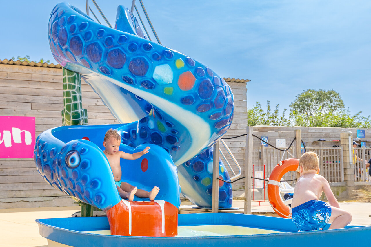Kinder spielen auf der blauen Wasserrutsche auf dem Campingplatz CAPFUN Falaises in Gonneville sur Mer.