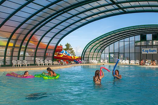 Überdachtes Schwimmbad, Rutsche und Kinder im CAPFUN Falaises Campingplatz Gonneville sur Mer.