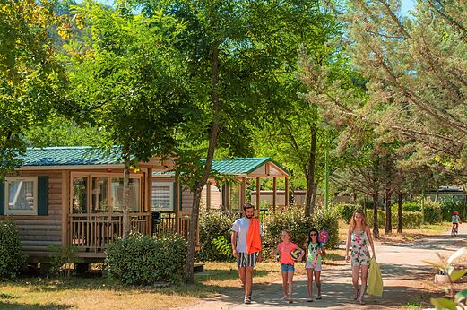 Houten stacaravans en familie wandelend op een pad op camping CLICOCHIC Filament in Thoiras (30).