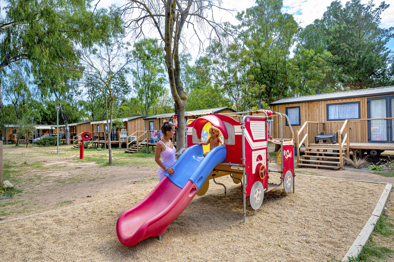 Spielplatz mit Zugrutsche, Kind und Mobilheimen auf dem Campingplatz CAPFUN Fleurs d'Agde in AGDE (34).