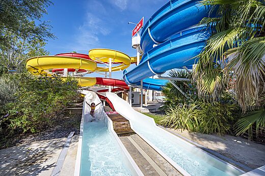 Kleurrijke waterglijbanen en kind glijdend op camping CAPFUN Fleurs d'Agde in AGDE (34).