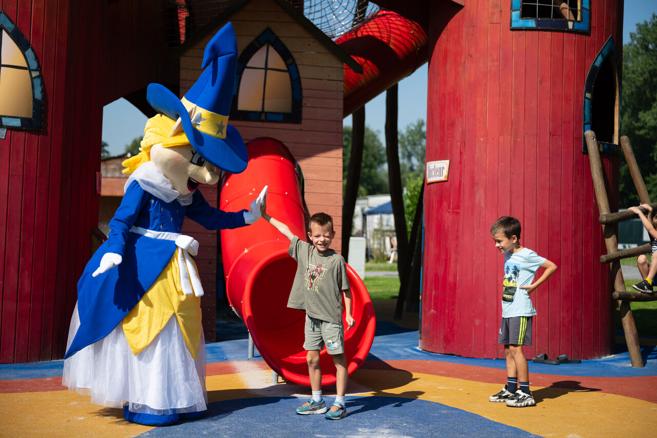Maskottchen und Kinder auf dem Spielplatz mit Rutsche am Campingplatz CAPFUN Fort Bedmar in Sint-Gillis-Waas.