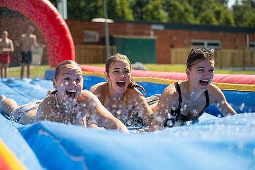 Jeunes femmes s'amusant sur un toboggan aquatique gonflable au camping CAPFUN Fort Bedmar à Sint-Gillis-Waas.
