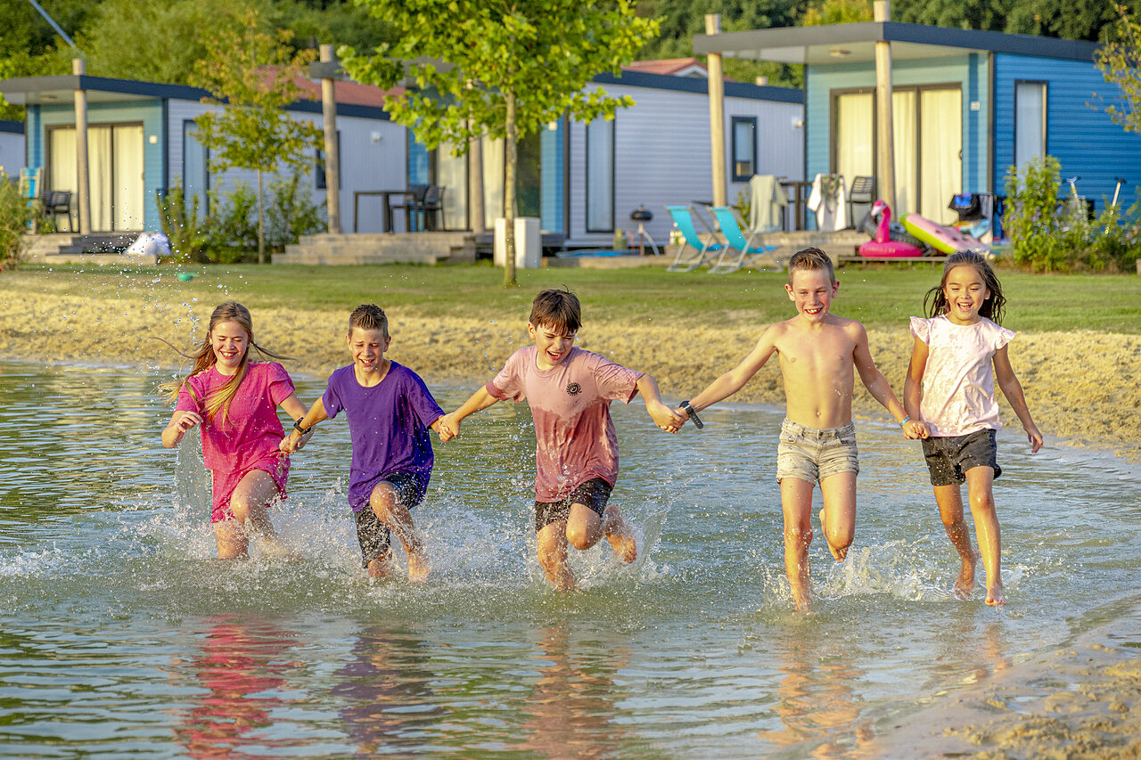 Fr�hliche Kinder rennen im seichten Wasser vor Mobilheimen auf dem Campingplatz CAPFUN De Fruithof in Klijndijk.