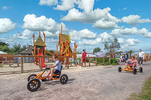 Kinderen op skelters en speeltuin op camping CAPFUN Golf in SAINT JEAN DE LA RIVIERE (50).
