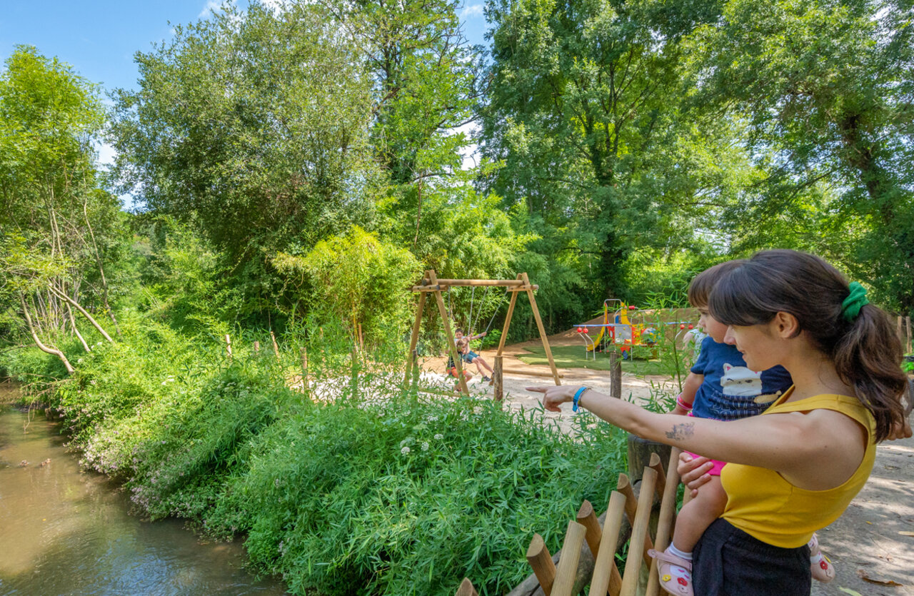 Playground with swings and children, riverbank at VAGUES OCEANES Granges campsite in GROLEJAC (24).