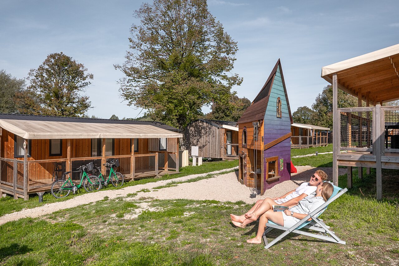 Paar entspannt bei Chalet und Spielplatz auf Camping CLICOCHIC Grisi�re in Clairvaux-les-Lacs (39).