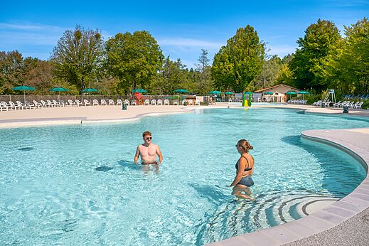 Groot buitenzwembad met stoelen en parasols op camping CLICOCHIC Grisière in Clairvaux-les-Lacs (39).