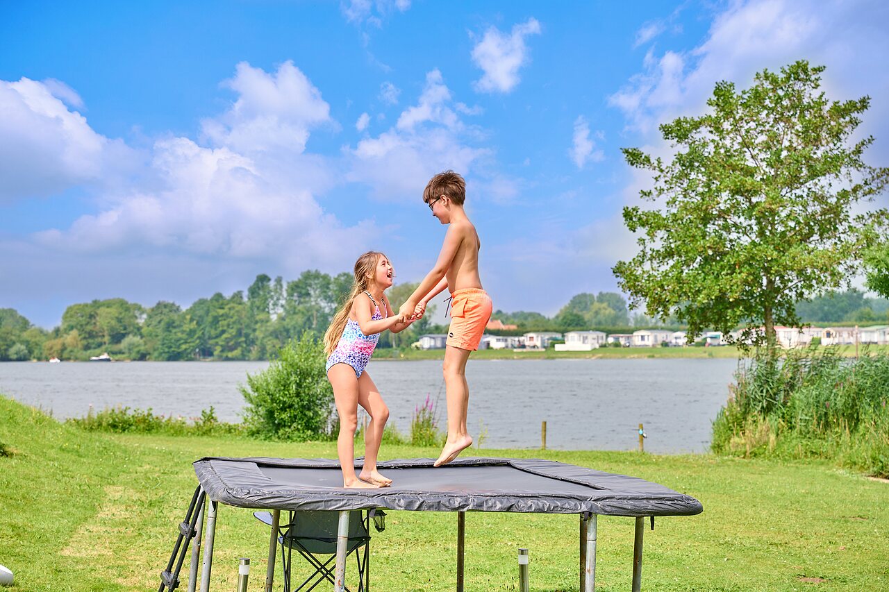 Zwei Kinder springen auf Au�entrampolin am See auf dem Campingplatz CAPFUN Groene Eiland in Appeltern.