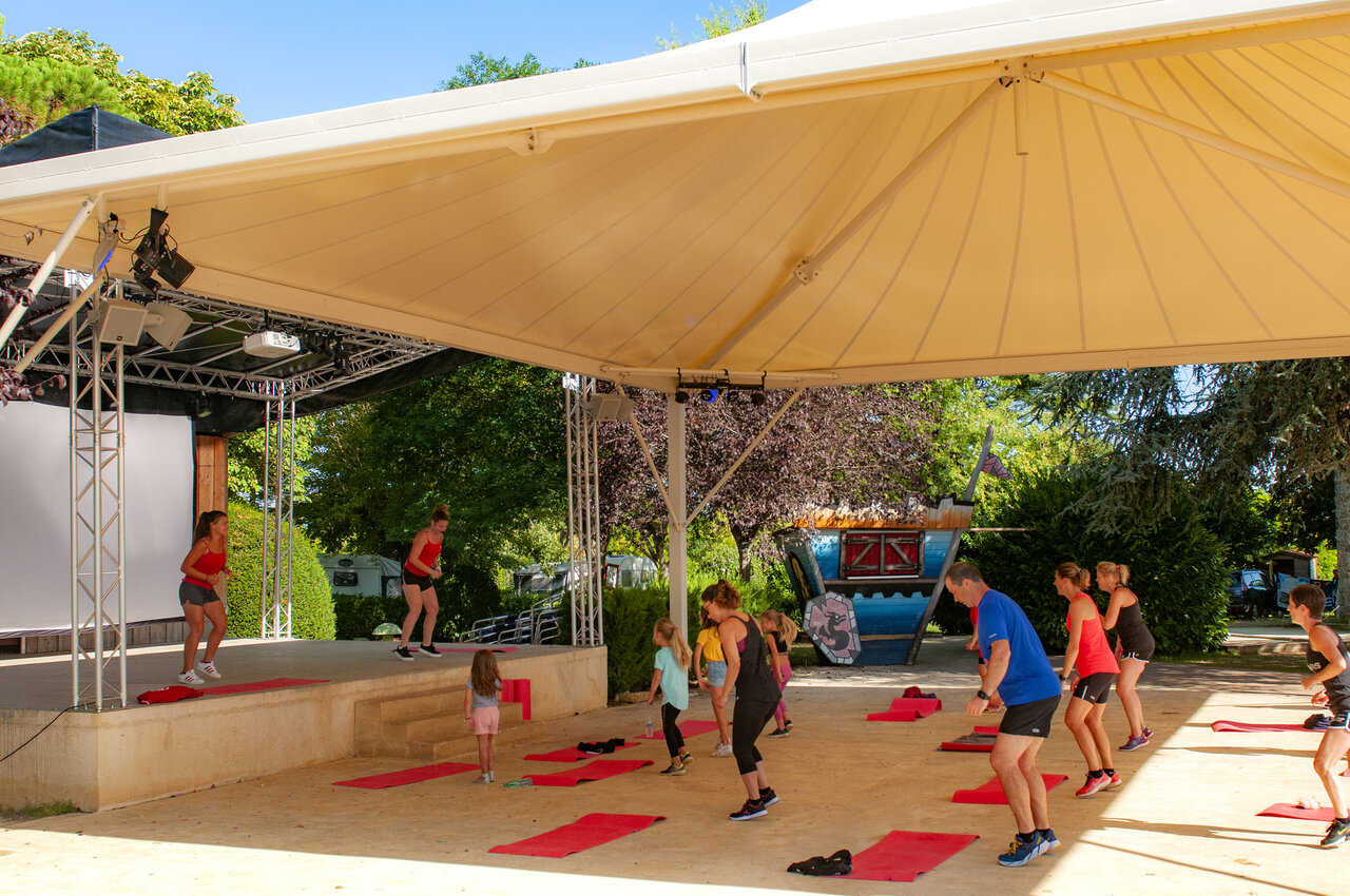 Outdoor fitness class on covered stage at CAPFUN Hauts de Ratebout campsite in STE FOY DE BELVES (24).