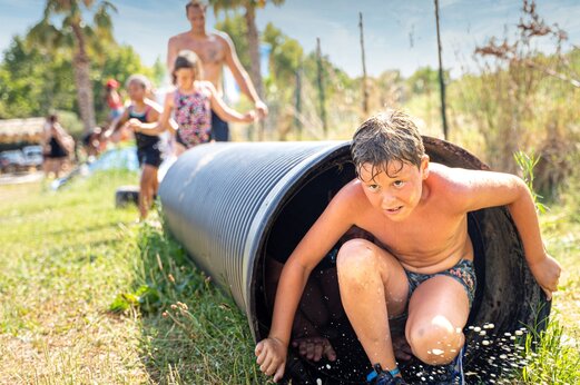 Kind kommt aus einem Wassertunnel, Spiel auf dem Campingplatz CAPFUN Hauts de Ratebout in STE FOY DE BELVES (24).
