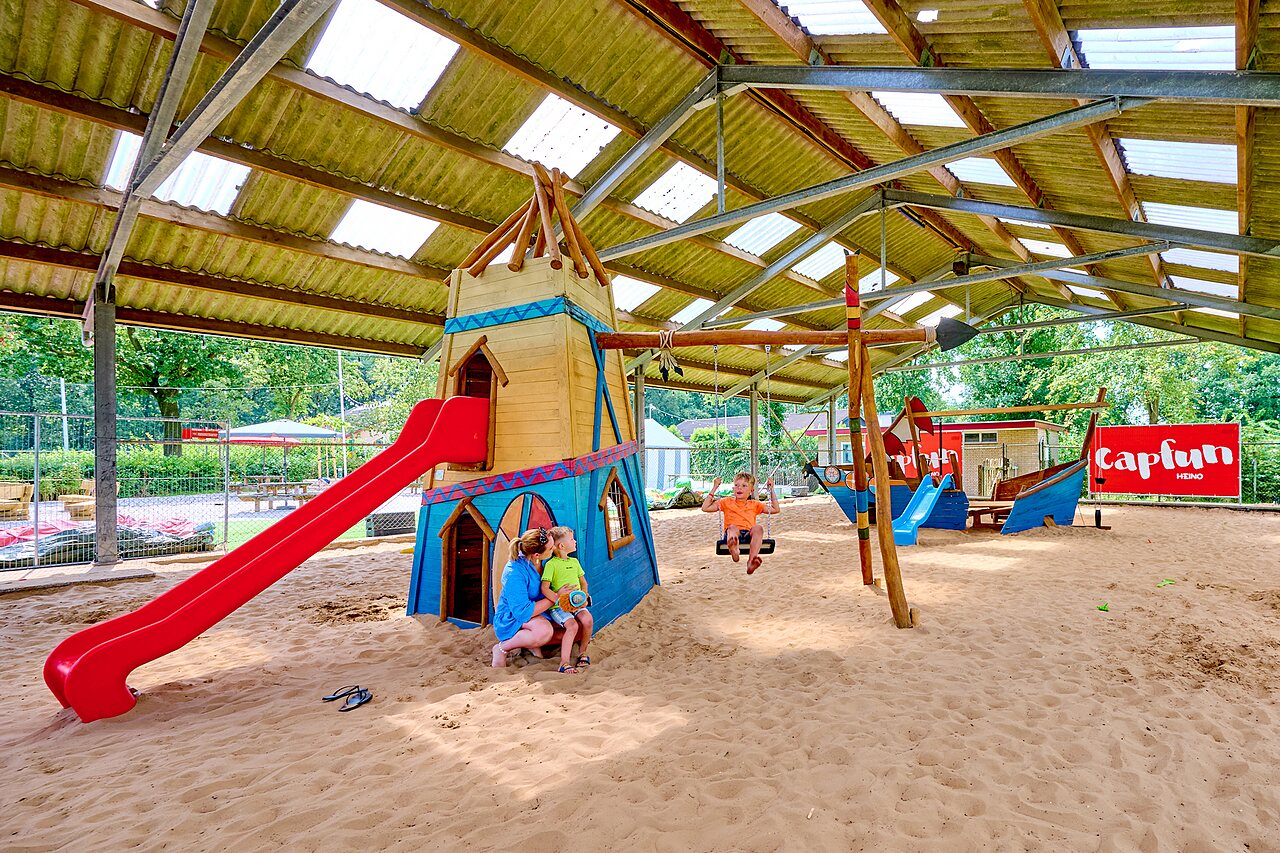 �berdachter Spielplatz mit Rutsche, Schaukeln und Sand am Campingplatz CAPFUN Heino in Heino.