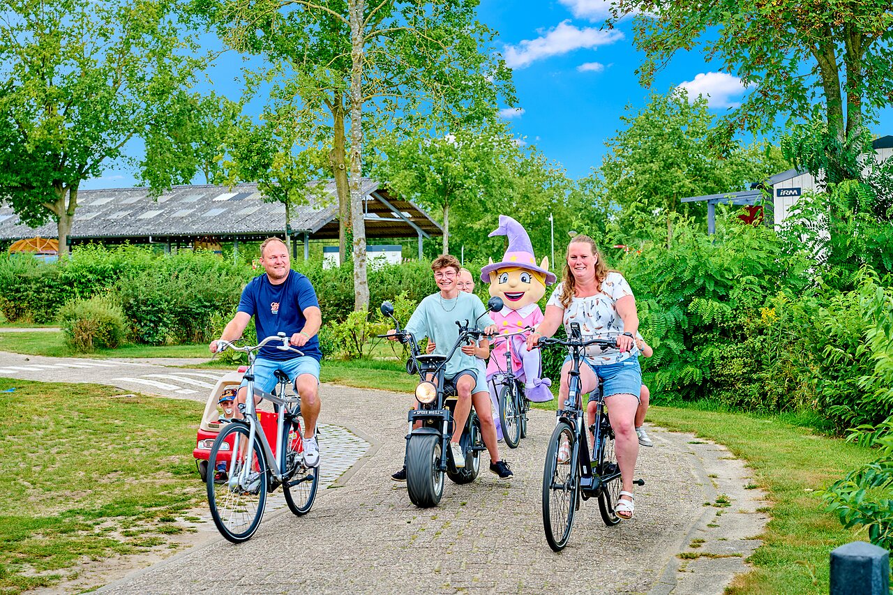 Familie und Maskottchen fahren Rad auf Weg auf Camping CAPFUN Heino in Heino.