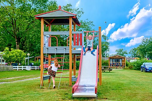 Spielplatz mit Rutsche und spielenden Kindern auf dem Campingplatz CAPFUN Heino in Heino.