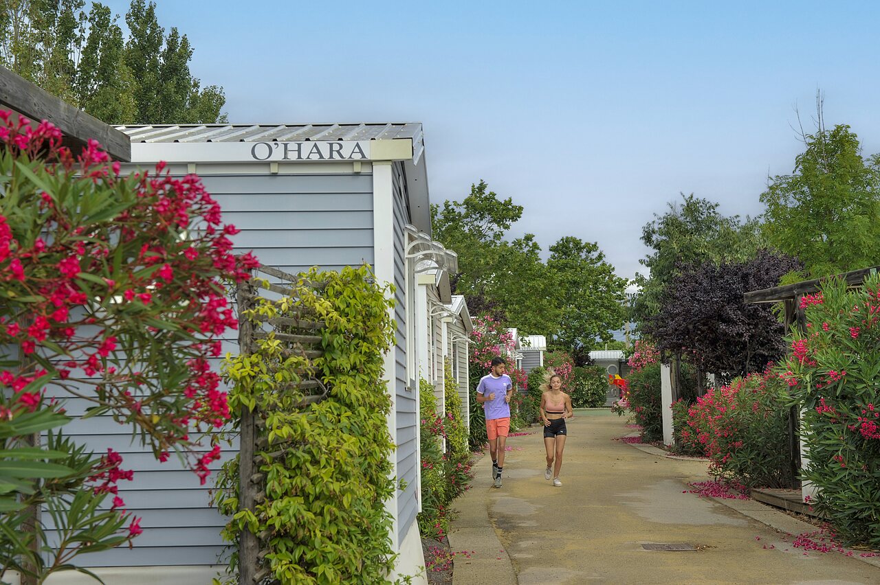 Joggers on flowery path, mobile homes at CAPFUN Hermitage in SERIGNAN.
