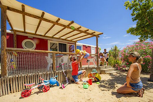 Rotes Mobil-home mit Terrasse, Familie und spielenden Kindern auf dem Campingplatz CAPFUN Hermitage in SERIGNAN (34).