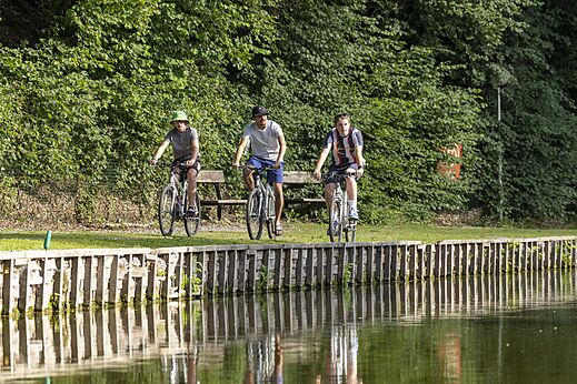 Drei Personen fahren Fahrrad entlang eines Gewässers auf Camping CAPFUN Hirondelle in Oteppe.