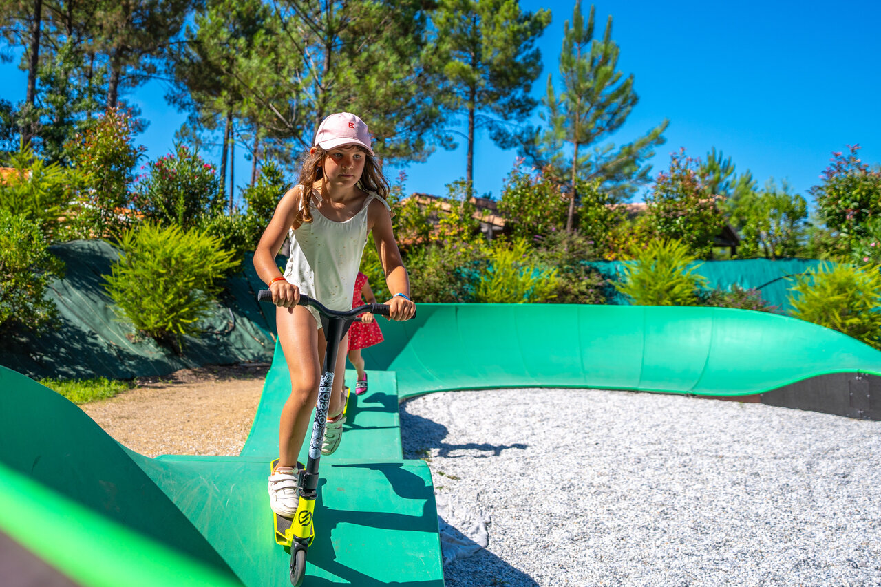 Kind auf Roller auf gr�nem Pumptrack am Campingplatz CAPFUN Huttes in Saint-Denis d'Ol�ron.