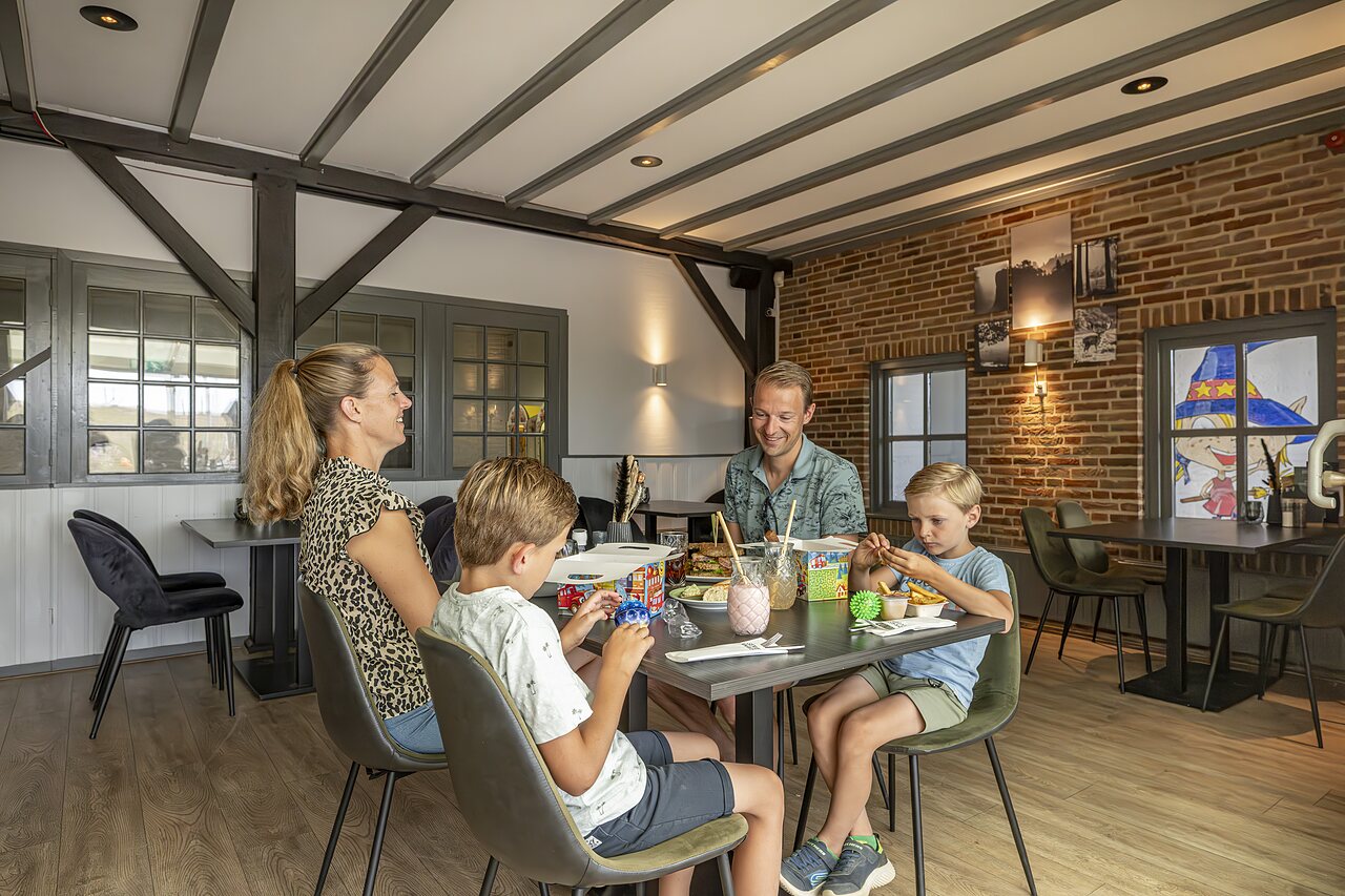 Familienrestaurant mit spielenden Kindern am Tisch auf dem Campingplatz CAPFUN IJsselstrand in Doesburg.