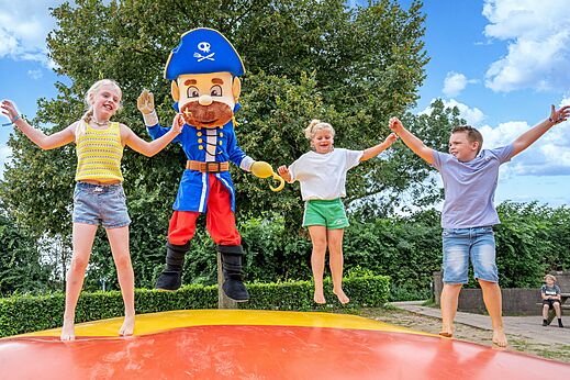 Kinder und Piratenmaskottchen springen auf Hüpfkissen am Campingplatz CAPFUN IJsselstrand in Doesburg.