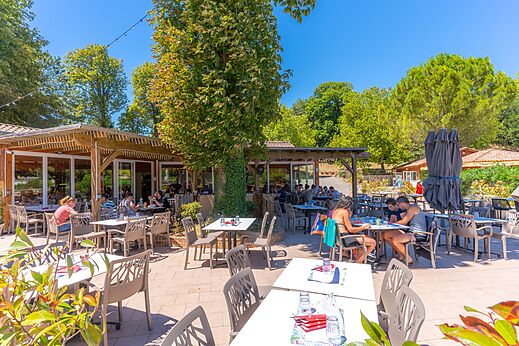 Sonnige Restaurantterrasse mit Gästen auf dem Campingplatz CAPFUN Imbours in LARNAS (07).