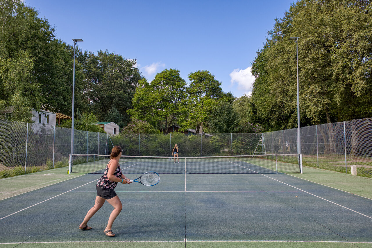 Cancha de tenis exterior con dos mujeres jugando en camping CLICOCHIC Lac de Miel, Beynat (19).