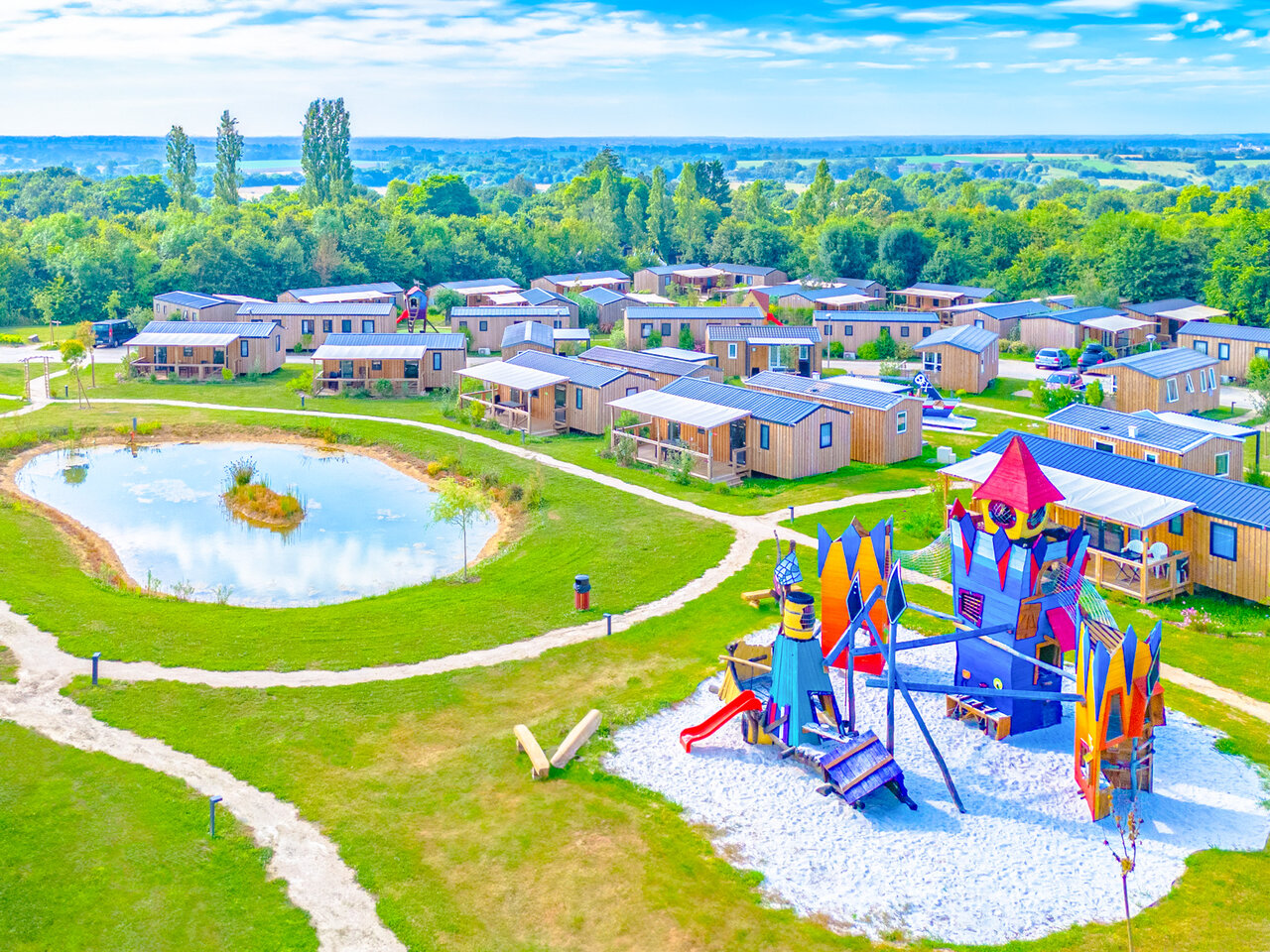 Bunter Spielplatz, Teich und Mobilheime auf dem Campingplatz CAPFUN Lac de Ribou in Cholet (49).