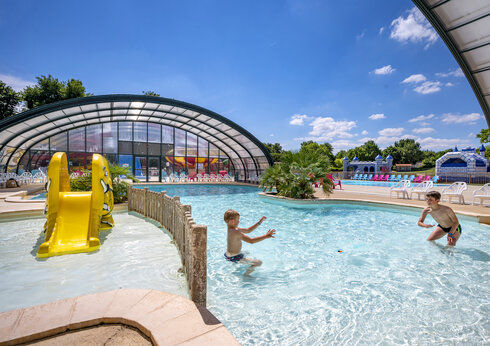 Piscina exterior, tobogán amarillo y niños en el camping CAPFUN Lac de Ribou.