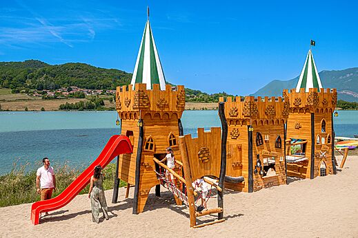 Holzschloss-Spielplatz mit roter Rutsche auf dem Campingplatz CLICOCHIC Lac du Lit du Roi in Massignieu-de-Rives (01).