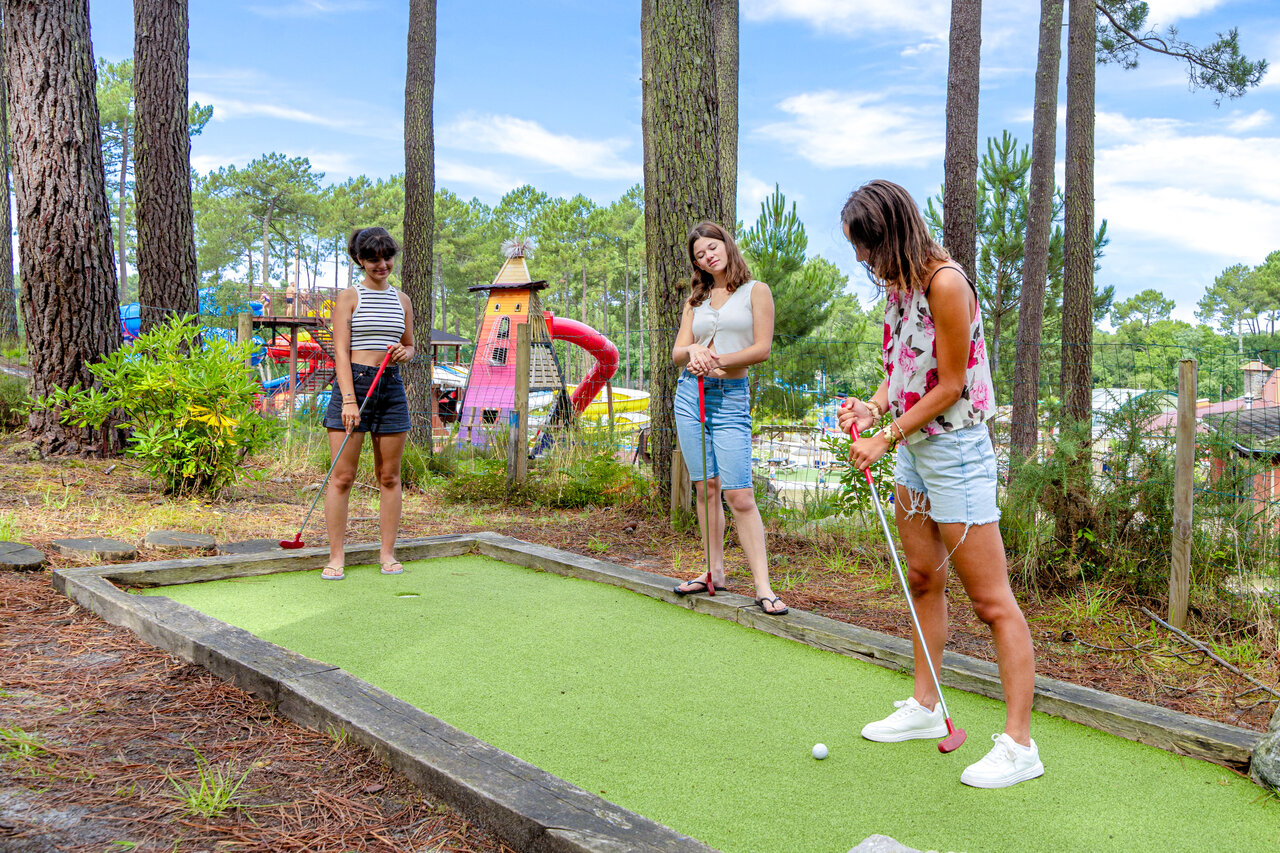 Minigolf met jonge vrouwen spelend, omringd door dennenbomen op camping CAPFUN Landisland in Moliets-et-Maa.