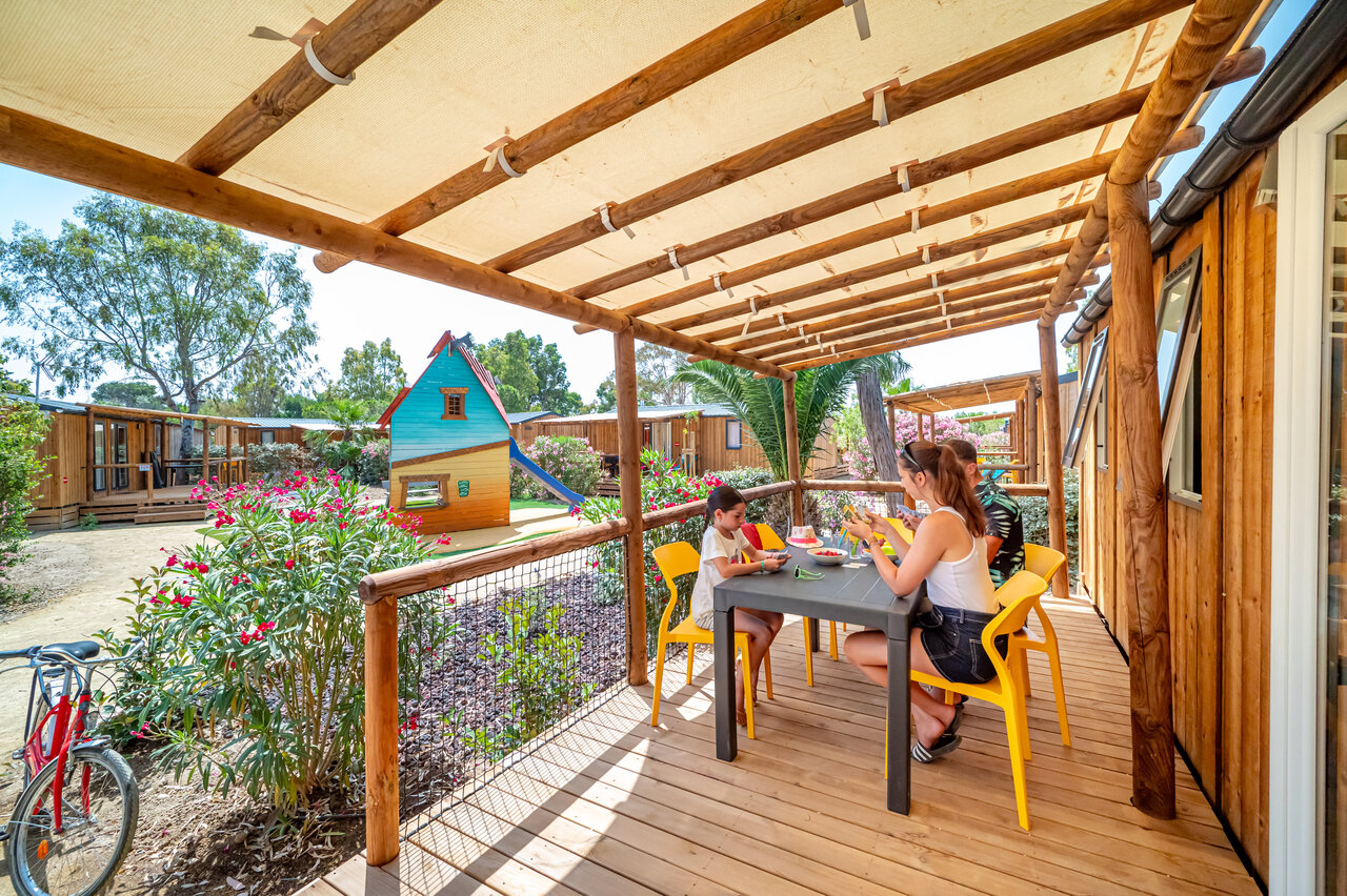 Familie isst auf Mobilheim-Terrasse mit Spielplatz auf Camping CAPFUN Las Bousigues in Le Barcar�s.