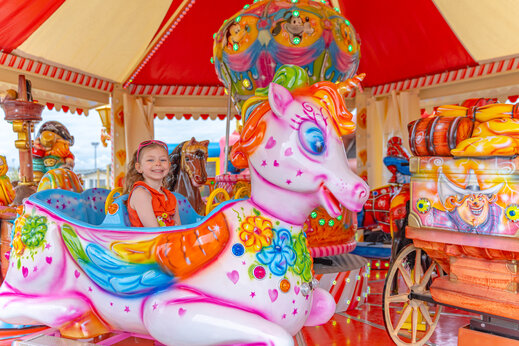 Petite fille souriante sur un manège licorne coloré au camping VAGUES OCEANES Licorne à Dunkerque (59).