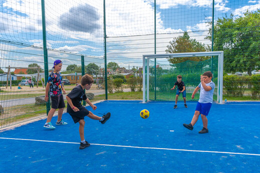 Enfants jouant au football sur le terrain multisport au camping VAGUES OCEANES Licorne à Dunkerque (59).