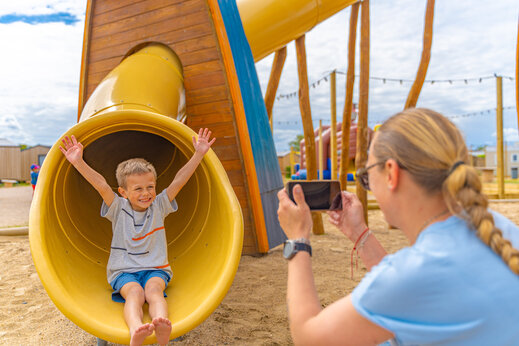 Enfant souriant sur un toboggan jaune dans l'aire de jeux au camping VAGUES OCEANES Licorne à Dunkerque (59).