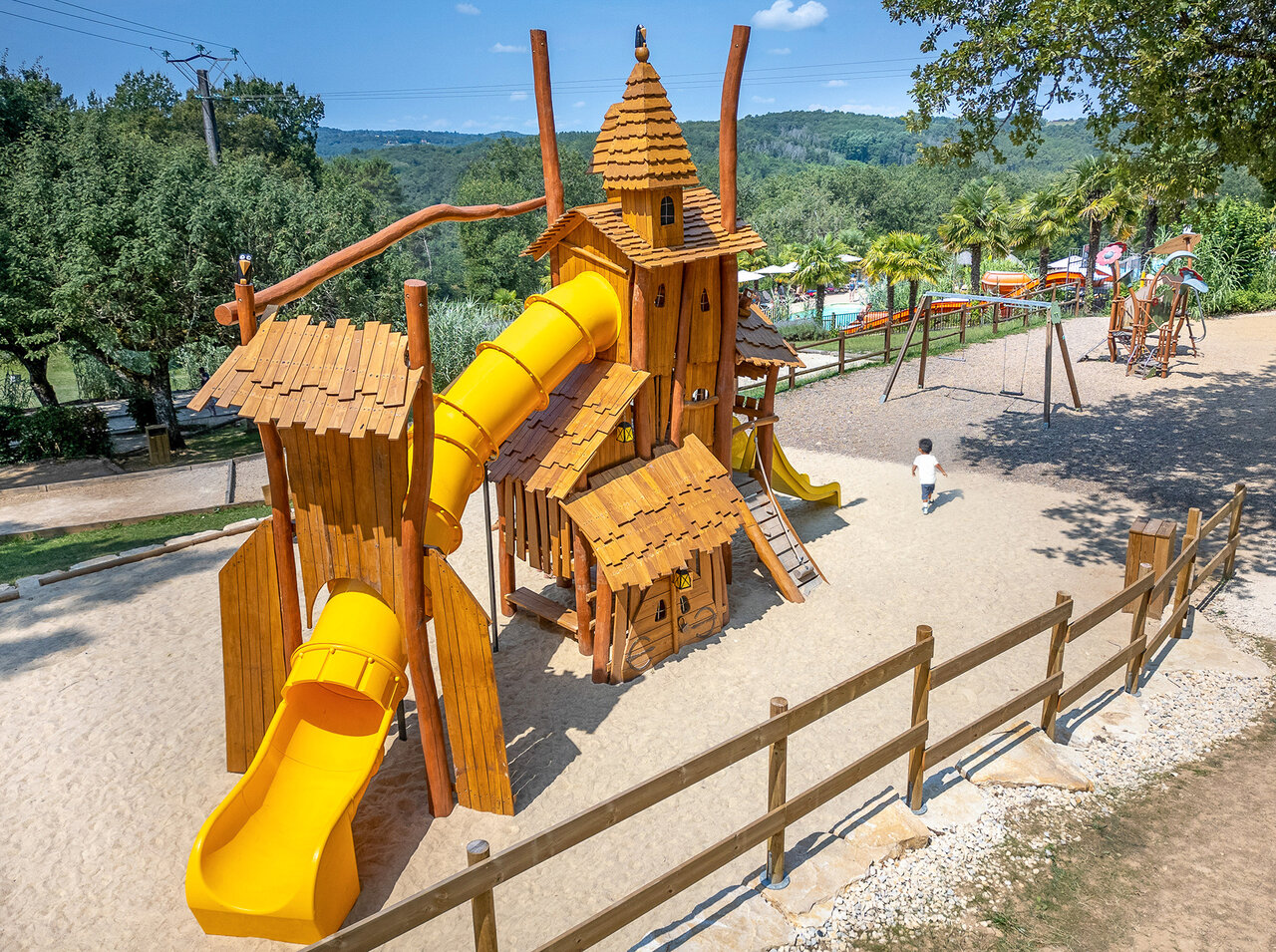 Wooden playground with yellow slides for children at CLICOCHIC Linotte campsite in Le Bugue (24).
